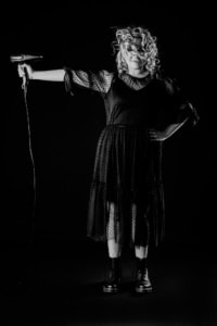 Haarstyling und Mode in Businessfotografie - photoart hübner business Frau mit Lockenfrisur und schwarzem Kleid hält einen Haartrockner, kreative Business- und Personal B.