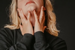 Moderne Businessfotografie für Selbstpräsentation - photoart hübner business Frau im Business-Outfit zeigt nachdenkliche Pose, Hände am Hals, dunkler Hintergrund.