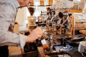 Kaffeebarista bei der Zubereitung von Espresso - photoart hübner business Mann bereitet Kaffee mit professioneller Espressomaschine zu, Fokus auf Barista-Arbeit im Café.