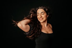 Porträt einer jungen Frau mit lockigem Haar, lächelnd, auf schwarzem Hintergrund. - photoart hübner business Lächelnde Frau mit lockigem Haar, Business- und Personal Branding-Foto.