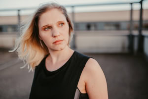 Porträt einer jungen Frau bei Business-Fotoshoot, professionelle Unternehmensfotografie. - photoart hübner business Frau mit blondem Haar und schwarzem Top blickt nach links, urbaner Hintergrund.