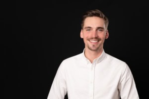 Freundliches Business-Porträt eines Mannes in weißem Hemd vor schwarzem Hintergrund.