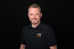 Hübscher Portrait eines Mitarbeiters bei Photoart Hübner Business - photoart hübner business Freundliches Portrait eines Mitarbeiters in schwarzem Polo-Shirt vor schwarzem Hintergrund.