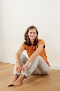 Moderne Businessfotografie für Personal Branding und Karriere. - photoart hübner business Hübsche Frau sitzt entspannt auf Holzboden, freundliches Lächeln, natürliche Beleuchtung.