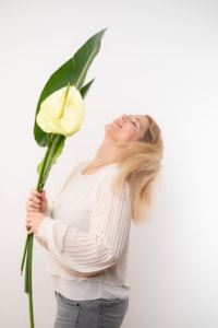 Blumenfotografie für Business & Personal Branding - photoart hübner business Frau hält große grüne Blätter und eine gelbe Blume, lächelnd und entspannt.