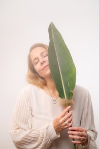 Blumenblatt-Model für Business- und Personal Branding Fotos - photoart hübner business Frau hält großes Blatt vor Gesicht, Fokus auf natürliche Eleganz und Selbstbewusstsein.