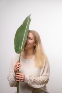 Moderne Businessfotografie mit natürlichem Ausdruck - photoart hübner business Frau hält große grüne Blätter vor Gesicht, professionelles Businessfoto.
