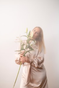 Moderne Businessfotografie mit Blumen - photoart hübner business Frau hält große Lilie in Business-Outfit vor hellem Hintergrund.