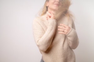 Businessfotografie Portrait bei Hübner - photoart hübner business Nahaufnahme einer Frau in einem beigen Pullover, die lächelnd ihre Haare berührt.