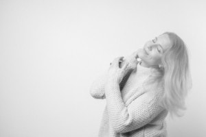 Strahlendes Lächeln einer Frau in einem Pullover - photoart hübner business Lächelnde Frau in einem Pullover, die ihre Schultern umarmt, symbolisiert Selbstvertrauen und Profes.