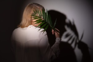 Businessfotografie mit Schatteneffekt - photoart hübner business Frau hält eine Palme vor das Gesicht, Schatten auf dunklem Hintergrund.