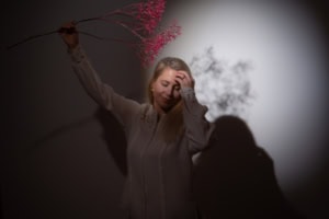 Businessporträt mit Blumenrequisite - photoart hübner business Frau hält Zweig mit pinken Blüten vor dunklem Hintergrund, kreative Businessfotografie.