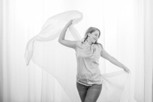 Businessfotografie mit lebendiger Bewegung - photoart hübner business Frau posiert dynamisch mit Tuch vor hellen Vorhängen, professionelle Businessfotografie.
