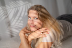 Hübsche junge Frau entspannt zu Hause, Lifestyle-Fotografie - photoart hübner business Entspannte junge Frau liegt auf dem Sofa, lächelt freundlich, in einem hellen, modernen Wohnraum.