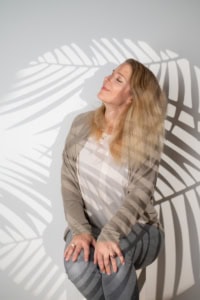 Businessfotografie mit natürlichem Licht und kreativen Schatteneffekten - photoart hübner business Frau in Businesskleidung posiert vor einer weißen Wand mit Schatten einer Palme, ideal für Personal.