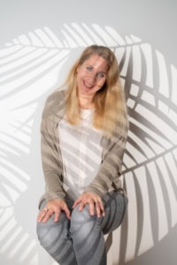 Businessfotografie Portrait einer lächelnden Frau vor Schattenwurf von Blättern - photoart hübner business Frau sitzt entspannt vor Schatten von Blättern, ideal für Business- und Personal Branding Fotos.