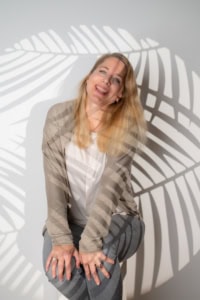 Businessfotografie Portrait mit natürlichem Lichteffekt - photoart hübner business Fröhliches Businessportrait einer Frau vor Schatten einer Palme, professionell fotografiert.