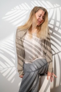 Porträt einer lächelnden Frau mit lockigem Haar vor einer weißen Wand mit Schatten von Blättern. - photoart hübner business Frau mit professionellem Business-Look, ideal für Personal Branding und Karrierefotos.