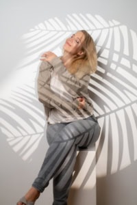 Moderne Portraitfotografie mit Schatteneffekt und natürlichem Ausdruck - photoart hübner business Frau sitzt auf Stuhl, Schatten von Palmblättern auf Hintergrund und Kleidung.