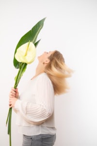 Businessfotografie Portrait mit Blumen - photoart hübner business Frau hält große grüne Blätter und eine gelbe Blume, professionelles Businessfoto.