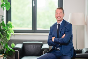 Businessfotograf im modernen Büro mit natürlichem Licht - photoart hübner business Mann in Businessanzug sitzt selbstbewusst im Büro, ideal für Unternehmens- und Personal Branding Fot.