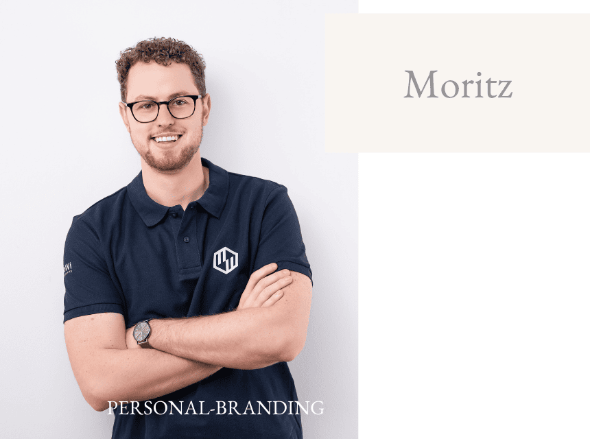 Mann mit Brille und freundlichem Lächeln, trägt dunkles Polo mit Logo, steht vor weißem Hintergrund.