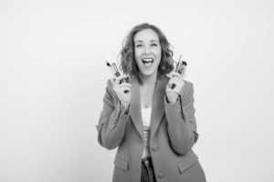 Porträt einer lachenden Frau mit Make-up-Produkten, Business- und Personal Branding. - photoart hübner business Lächelnde Frau hält Make-up-Pinsel und Lippenstift, ideal für Business- und Karrierefotografie.