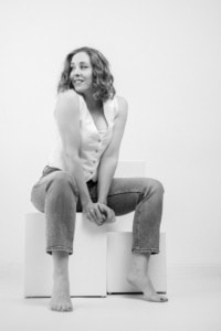 Porträt einer jungen Frau in Businesskleidung, sitzend auf weißen Quadern, in einem professionellen Fotoshooting. - photoart hübner business Frau in Businessoutfit, lächelnd, in einem Studio mit neutralem Hintergrund.