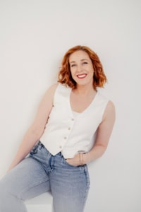 Moderne Businessporträtaufnahme einer jungen Frau mit roten Locken, lächelnd vor neutralem Hintergrund. - photoart hübner business Businessporträt einer Frau mit roten Locken, freundlichem Lächeln, in professionellem Umfeld.