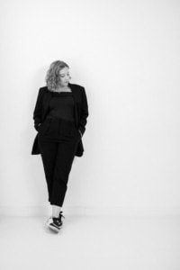 Moderner Business-Look mit Sneakers vor weißer Wand - photoart hübner business Frau in Businessoutfit mit Sneakers lehnt an weißer Wand, professionell und modern.