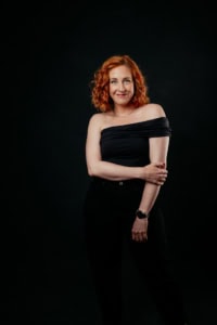 Businessfotografie Portrait einer Frau vor dunklem Hintergrund - photoart hübner business Porträt einer Frau mit roten Locken, professionell fotografiert für Business- und Personal Branding.