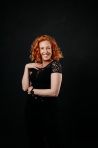 Porträt einer lachenden Frau mit roten Locken vor dunklem Hintergrund - photoart hübner business Lachende Frau mit roten Locken, professionelles Business-Porträt, Fotografie von Photoart Hübner Bus.