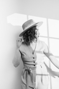 Moderne Businessfrau bei Fotoshooting in natürlichem Licht - photoart hübner business Businessfrau posiert mit Hut vor Fenster, professionelle Unternehmensfotografie.