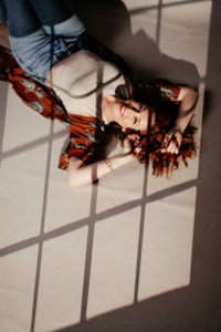 Selbstbewusstes Portrait einer jungen Frau - photoart hübner business Frau liegt auf Boden im Sonnenlicht, lächelt und posiert für Business- und Personal Branding Fotos.