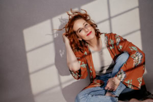 Porträt einer jungen Frau mit roten Locken, lächelnd, in natürlichem Licht, für Business- und Personal Branding Fotos. - photoart hübner business Frau mit roten Locken, lächelnd, in natürlichem Licht, geeignet für Business- und Karrierefotografie.