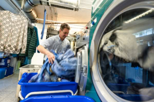 Wäsche waschen in der Wäscherei - photoart hübner business Mann sortiert Kleidung in der Wäscherei, professionelle Textilpflege für Unternehmen.